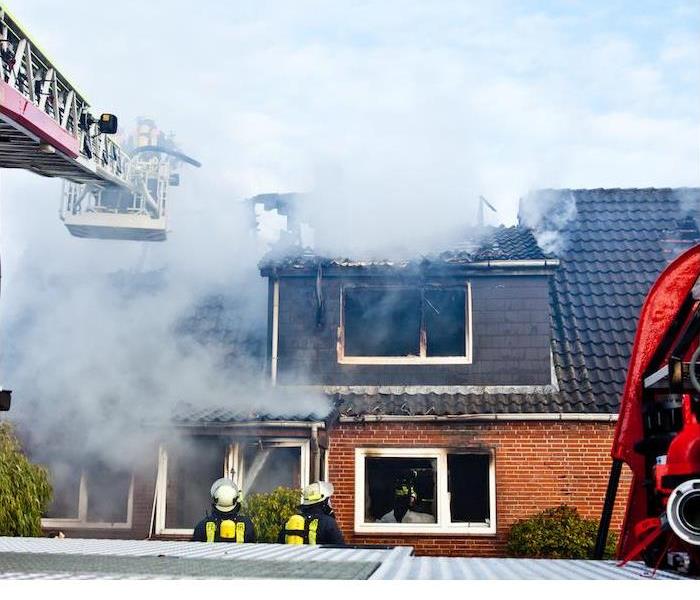 fire fighters spraying water into flames of red brick home