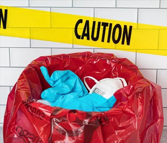 yellow caution tape with discarded gloves and mask in a red biohazard bag